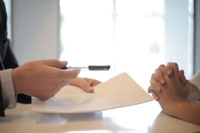 Hands passing a signed document across a bright desk